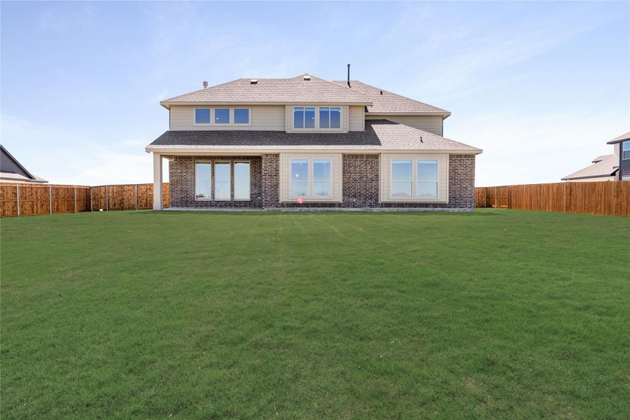Rear view of two-story brick home with large fenced backyard and green lawn Rear view of two-story brick home with large fenced backyard and green lawn