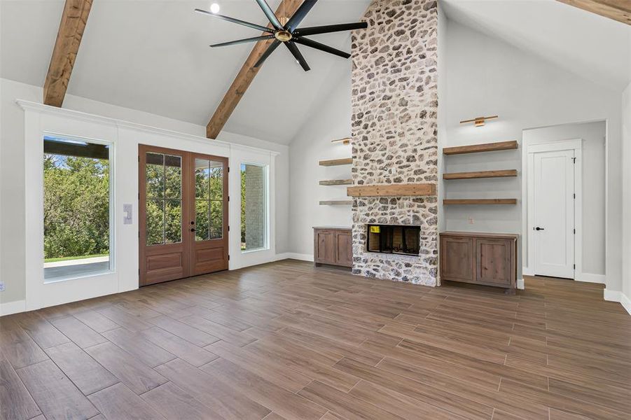 Unfurnished living room with high vaulted ceiling, french doors, wood tiled floors, a stone fireplace, and ceiling fan Unfurnished living room with high vaulted ceiling, french doors, wood tiled floors, a stone fireplace, and ceiling fan