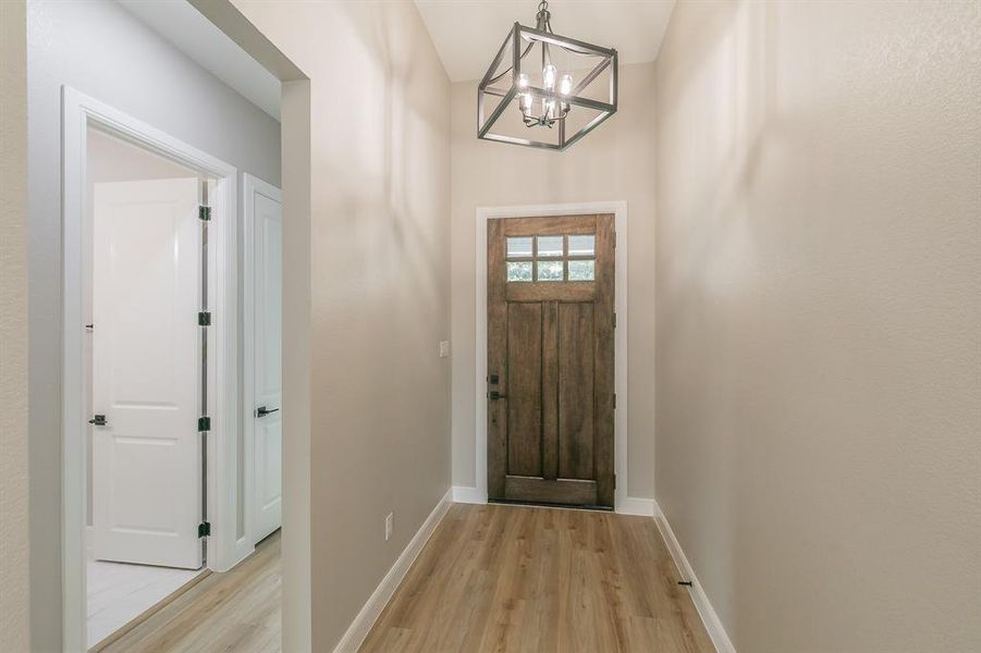 Entryway featuring light wood finished floors, a chandelier, and baseboards Entryway featuring light wood finished floors, a chandelier, and baseboards