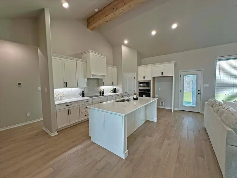 Kitchen with a breakfast bar, recessed lighting, beam ceiling, a center island with sink, and white cabinets Kitchen with a breakfast bar, recessed lighting, beam ceiling, a center island with sink, and white cabinets