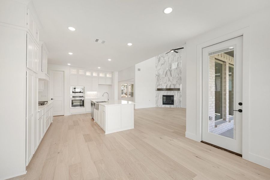 Open-concept kitchen with white cabinets, center island, and marble fireplace on light hardwood floors