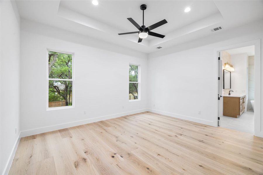Primary bedroom featuring a raised ceiling, engineered white oak floors, a ceiling fan, and ensuite bath. Primary bedroom featuring a raised ceiling, engineered white oak floors, a ceiling fan, and ensuite bath.