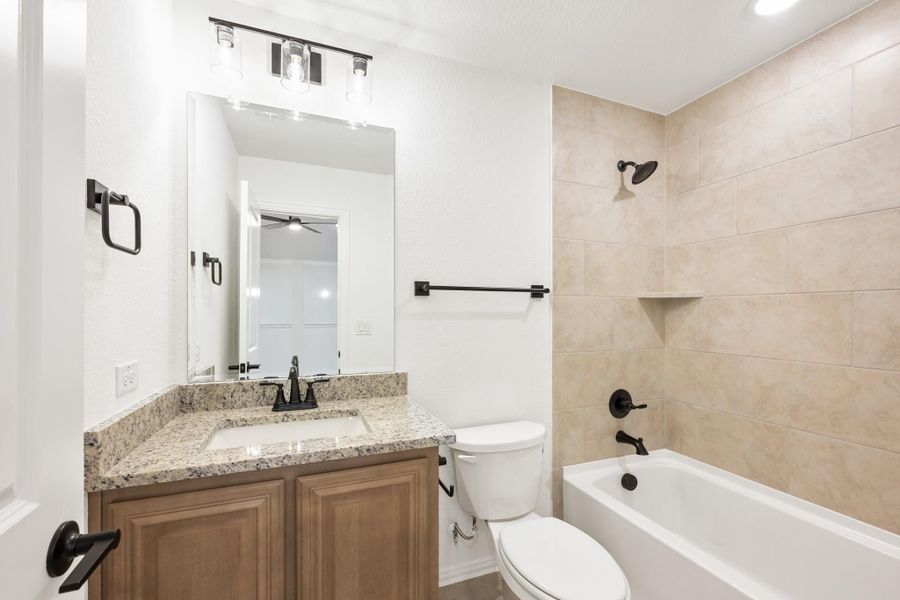 Bathroom with granite vanity, wood cabinets, and tub-shower combo with beige tile surround and black fixtures Bathroom with granite vanity, wood cabinets, and tub-shower combo with beige tile surround and black fixtures