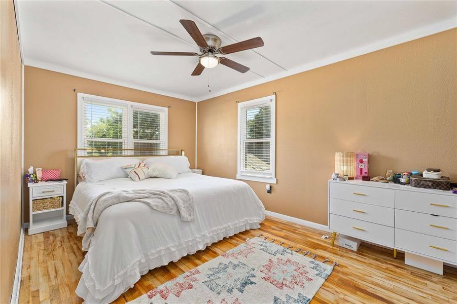 Bedroom with light wood finished floors, ornamental molding, and a ceiling fan Bedroom with light wood finished floors, ornamental molding, and a ceiling fan