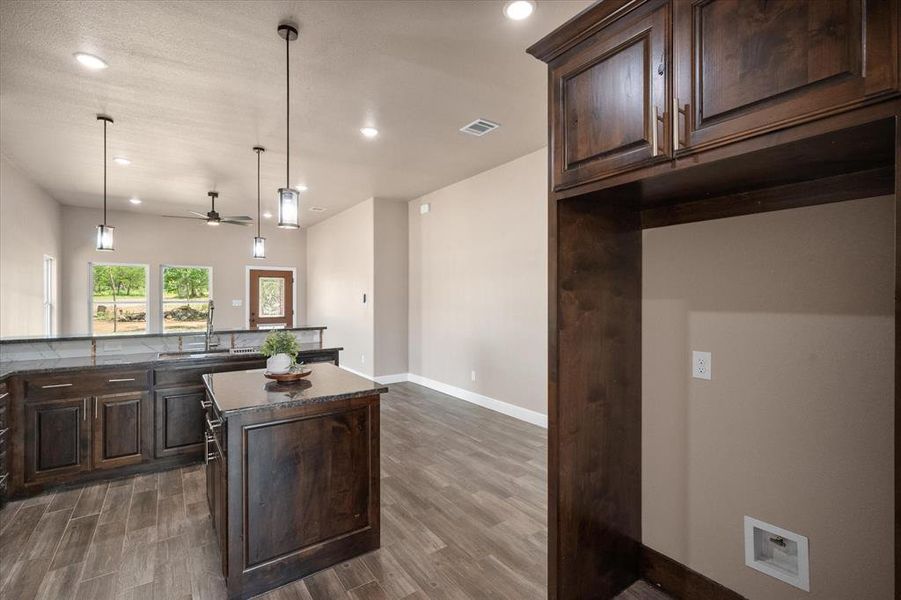 Open-concept living area featuring rich wood-finish cabinetry, dark granite countertops, and wood-look flooring