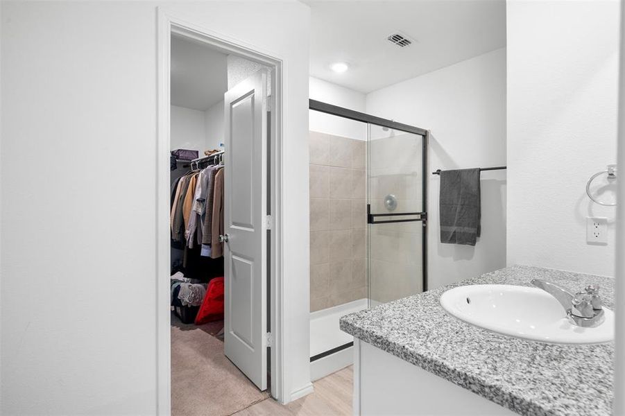 Full bathroom with a stall shower, vanity, a spacious closet, and light wood-style flooring Full bathroom with a stall shower, vanity, a spacious closet, and light wood-style flooring