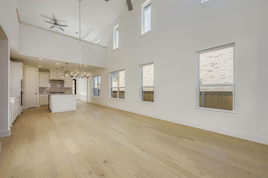 Unfurnished living room with ceiling fan, light wood-style flooring, healthy amount of natural light, a chandelier, and a high ceiling