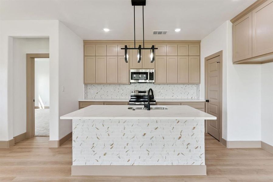 Kitchen featuring backsplash, light stone countertops, hanging light fixtures, stainless steel appliances, and a center island with sink Kitchen featuring backsplash, light stone countertops, hanging light fixtures, stainless steel appliances, and a center island with sink