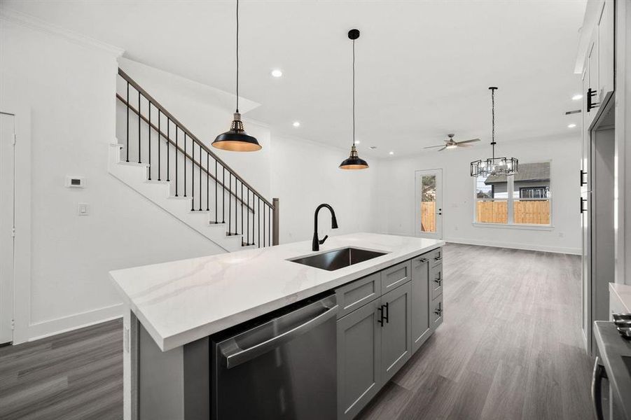 A view of the island featuring the dishwasher, the elegant staircase, luxurious vinyl plank flooring, and a peak of the living area. Did you catch a glimpse of those fabulous two-toned cabinets in the kitchen?