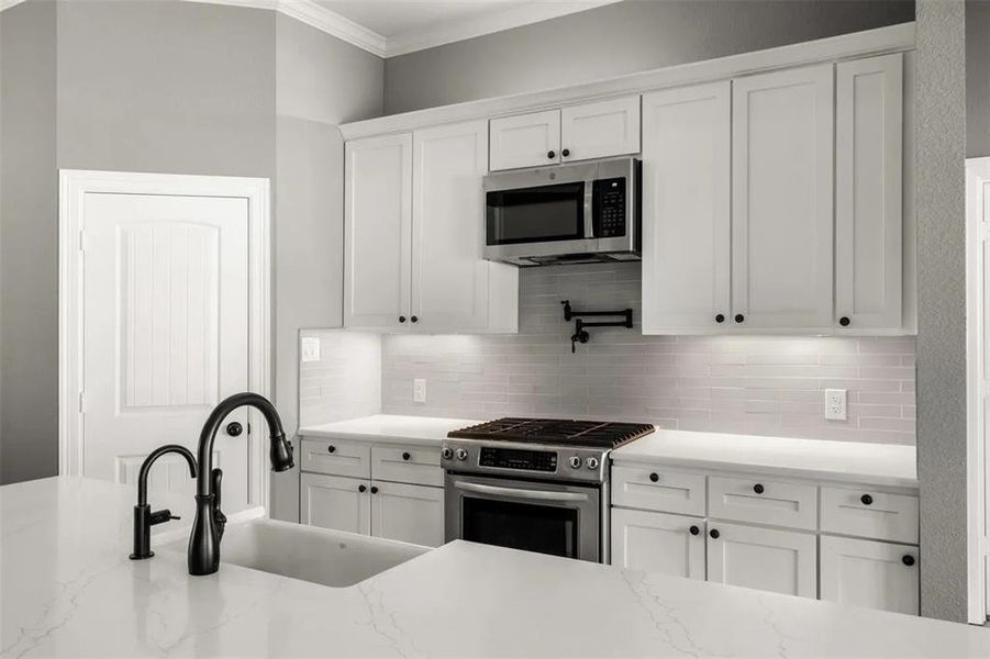 Kitchen featuring stainless steel appliances, white cabinets, light stone counters, and backsplash