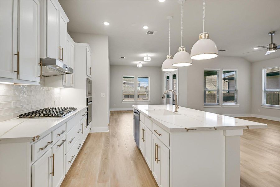 An open floor plan integrates a modern kitchen with natural wood-toned flooring and stone counters. An open floor plan integrates a modern kitchen with natural wood-toned flooring and stone counters.