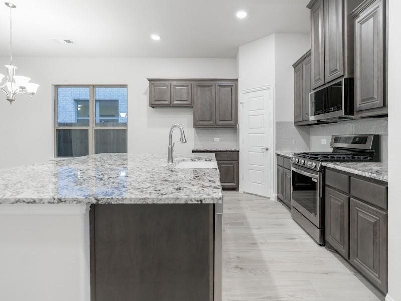 Kitchen featuring sink, tasteful backsplash, an island with sink, pendant lighting, and stainless steel appliances