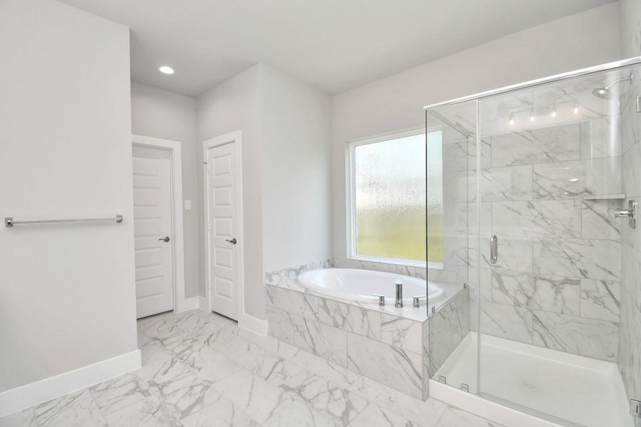 Indulge in a spa-like retreat within the confines of this primary bathroom. Delight in a spacious walk-in shower enveloped in stylish tile surround and unwind in a separate garden tub adorned with custom detailing. Sample photo of completed home with similar floor plan. Actual colors and selections may vary.