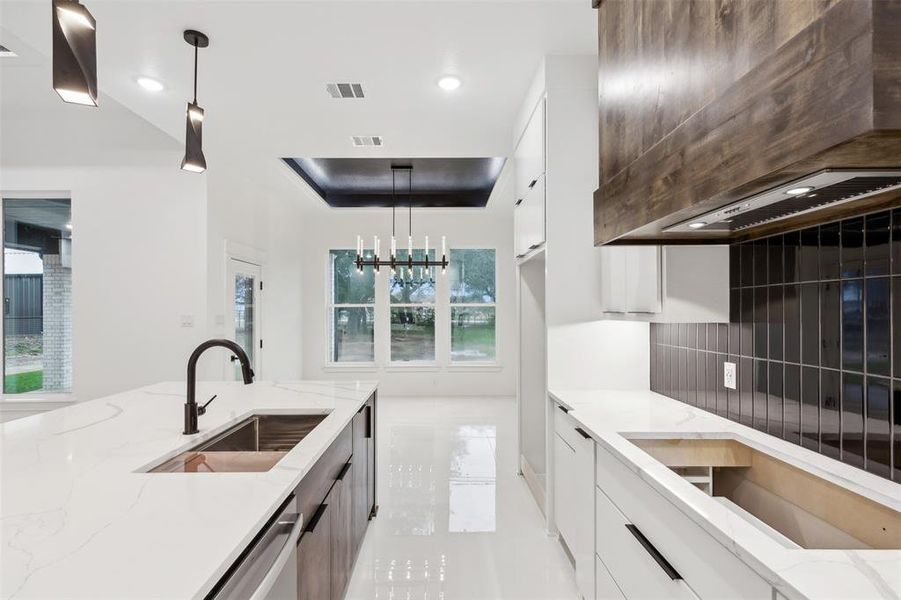 Kitchen with white cabinetry, sink, light stone countertops, pendant lighting, and decorative backsplash