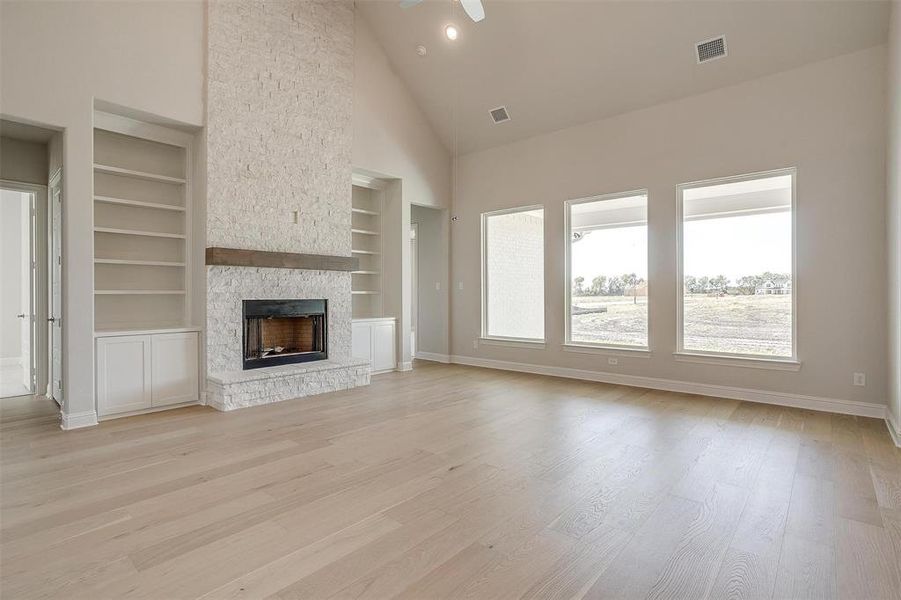 Unfurnished living room with a stone fireplace, built in features, light wood-type flooring, high vaulted ceiling, and ceiling fan