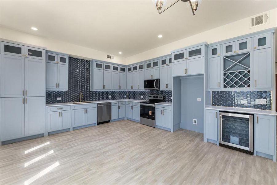 Kitchen with beverage cooler, stainless steel appliances, light countertops, decorative backsplash, and light wood-style flooring