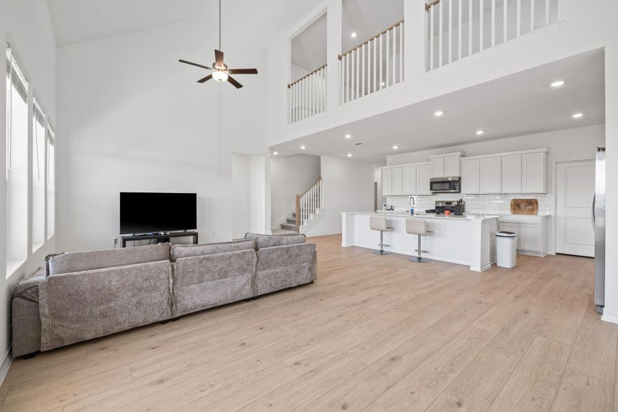 Living room featuring a ceiling fan, stairway, light wood-style floors, and a high ceiling