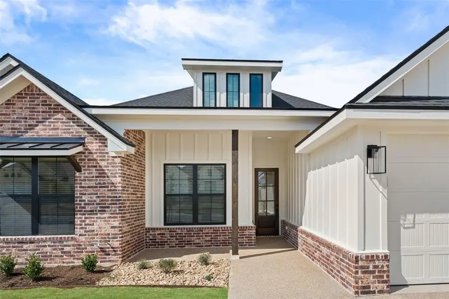 Entrance to property featuring board and batten siding, a porch, brick siding, and roof with shingles