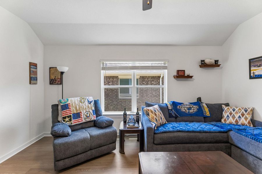 Living area featuring wood-finish flooring, white walls, and a large window with blinds
