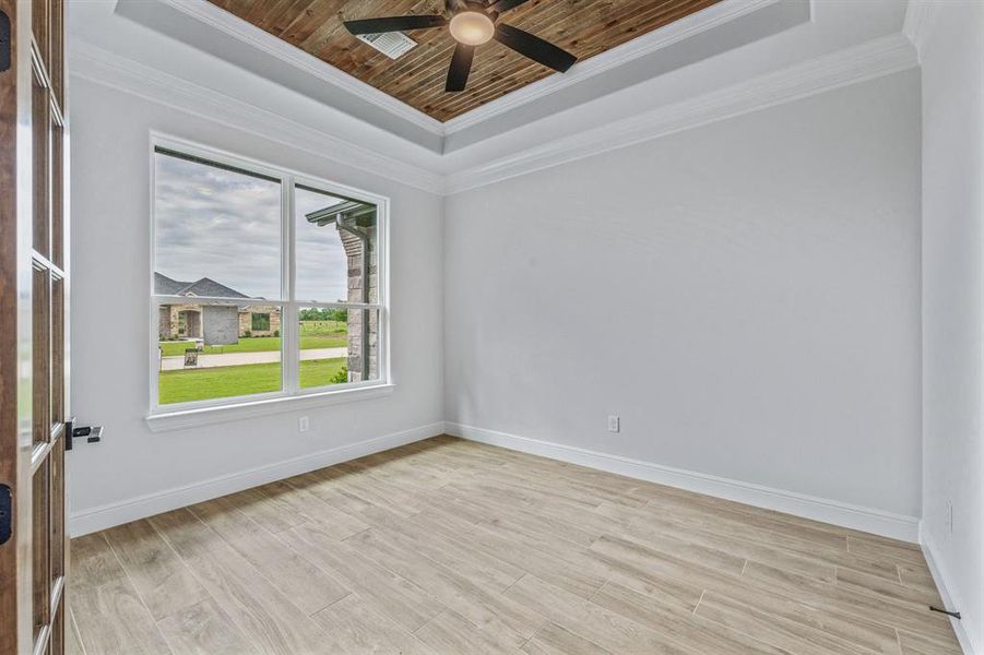 Unfurnished room featuring a raised ceiling, a ceiling fan, wood ceiling, light wood finished floors, and crown molding