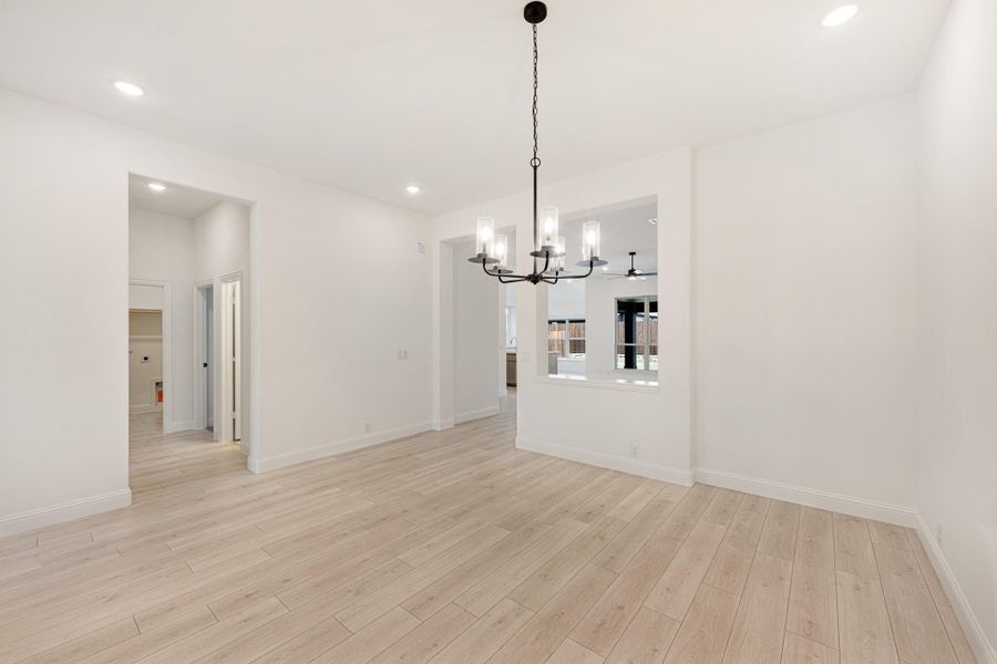 Empty dining room with light wood floors, white walls, and a black chandelier overhead