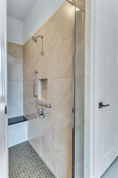 Walk-in shower with light-toned rectangular wall tiles, hexagonal floor tiles, a built-in bench with a dark countertop, a recessed niche, and grab bars Walk-in shower with light-toned rectangular wall tiles, hexagonal floor tiles, a built-in bench with a dark countertop, a recessed niche, and grab bars