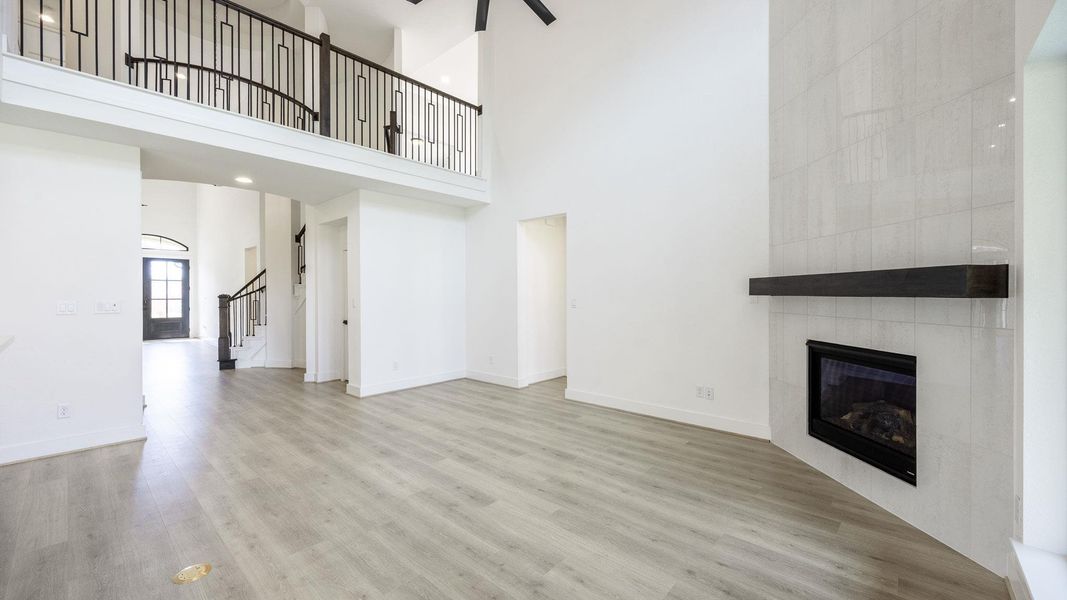 Unfurnished living room featuring light wood-type flooring, a tile fireplace, stairs, and a towering ceiling
