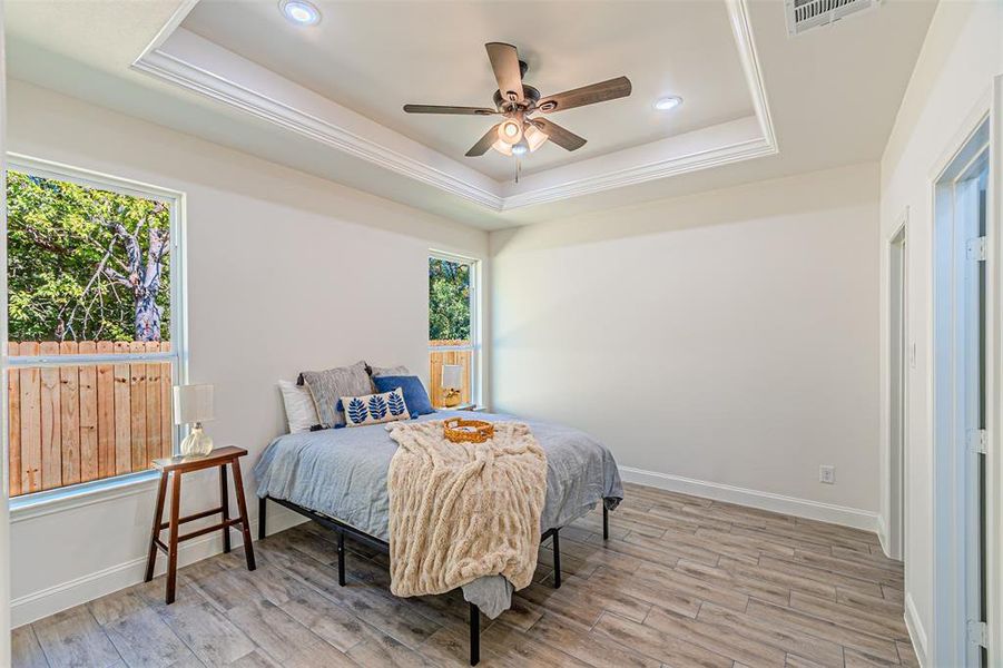 Bedroom with a tray ceiling, light wood-style flooring, ceiling fan, and recessed lighting