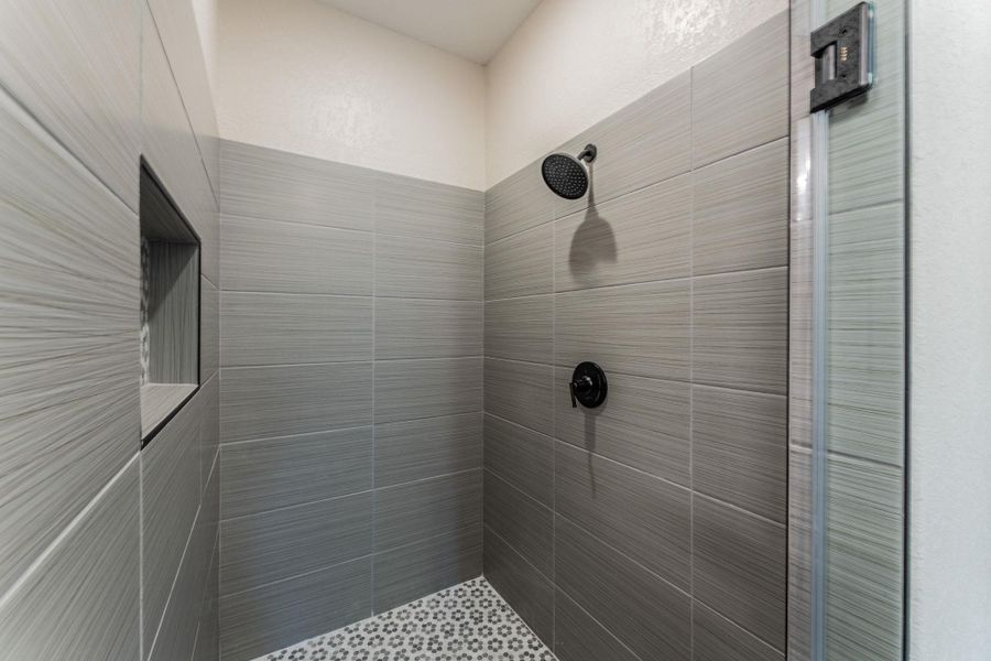Shower enclosure featuring gray horizontal tile, a built-in shower niche, matte black fixtures, a rain shower head, and a patterned mosaic tile floor