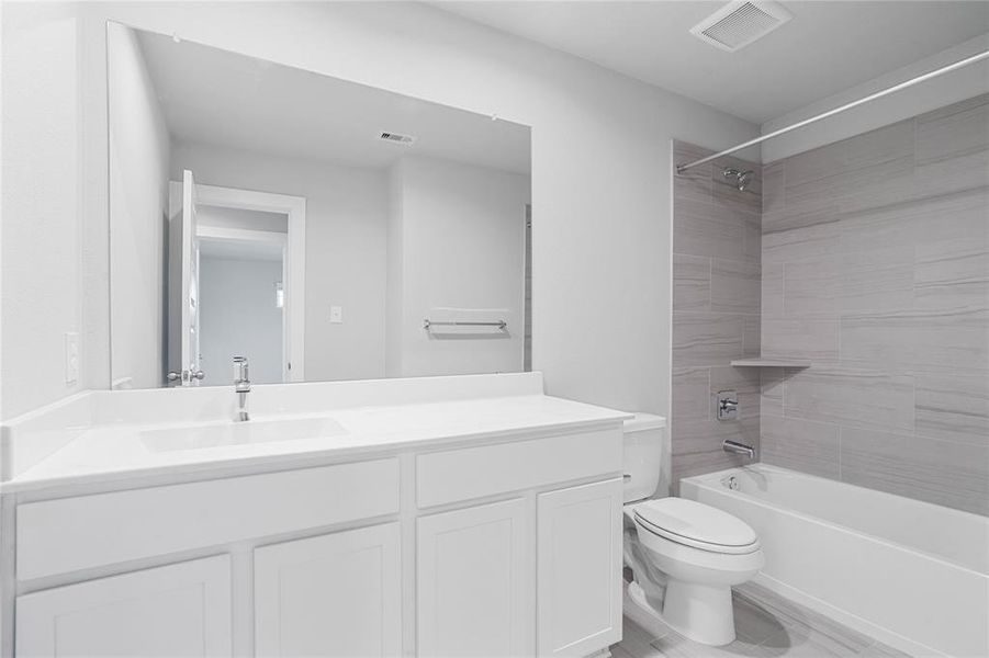 Secondary bath features tile flooring, bath/shower combo with tile surround, white stained wood cabinets, beautiful light countertops, mirror, dark, sleek fixtures and modern finishes.