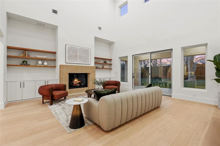 Living area featuring built in features, light wood-style flooring, a glass covered fireplace, and a high ceiling