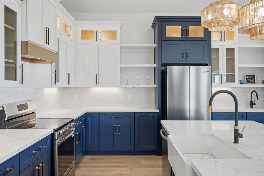 This modern kitchen features elegant navy and white cabinetry, stainless steel appliances, and marble countertops. The large island with a farmhouse sink and stylish pendant lighting adds a chic touch to the space.
