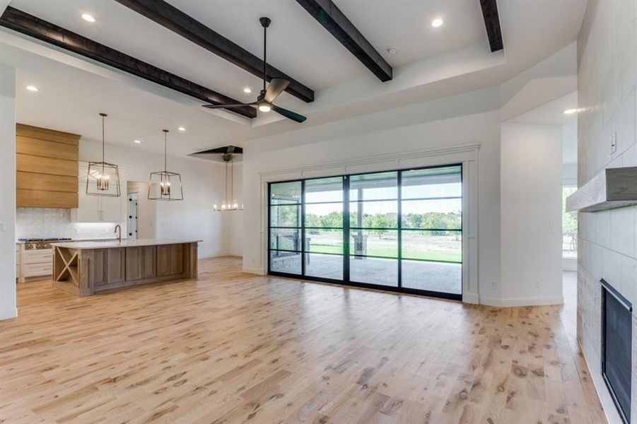 Unfurnished living room featuring ceiling fan with notable chandelier, a fireplace, beamed ceiling, light wood-type flooring, and sink