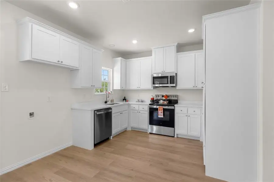 Kitchen featuring appliances with stainless steel finishes, white cabinetry, light wood-type flooring, and recessed lighting