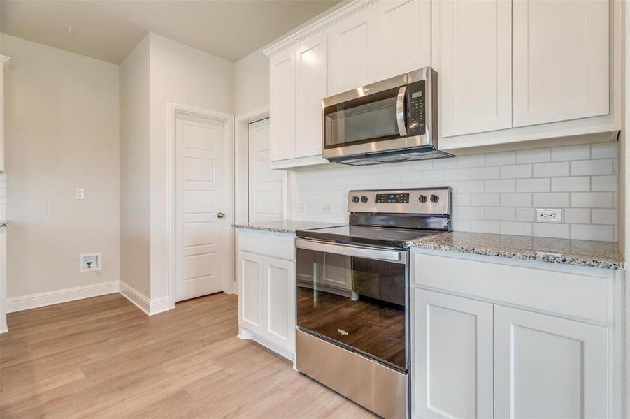 Kitchen featuring appliances with stainless steel finishes, backsplash, white cabinetry, and light stone counters