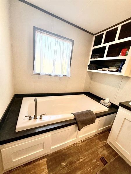 Bathroom with a garden tub, dark wood-style flooring, vanity, and ornamental molding