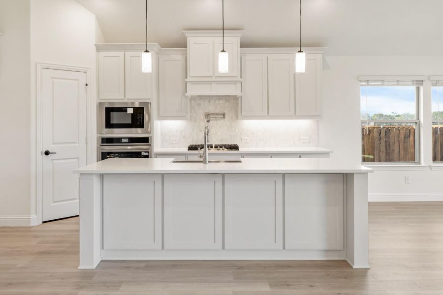 White kitchen with large island, pendant lights, stainless steel appliances, and light hardwood floors White kitchen with large island, pendant lights, stainless steel appliances, and light hardwood floors