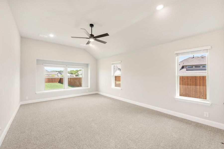 Empty bedroom with vaulted ceiling, ceiling fan, carpet flooring, and multiple windows Empty bedroom with vaulted ceiling, ceiling fan, carpet flooring, and multiple windows
