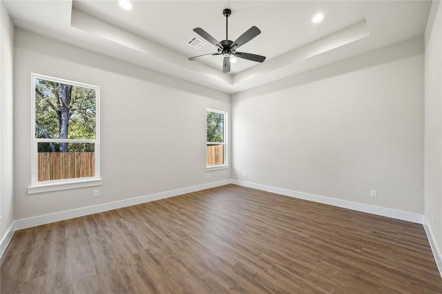 Empty room featuring a tray ceiling, wood finished floors, a ceiling fan, and recessed lighting