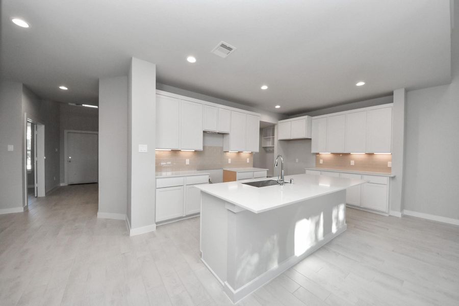 This generously spacious kitchen is a dream realized! With a massive granite island, high ceilings, soft close cabinets, granite countertops, stainless steel appliances, a sleek tile backsplash, recessed lighting, and an extended counter area, it offers both style and practicality. All this opens up to the expansive family room, creating a perfect hub for gatherings. Sample photo of completed home with similar floor plan. Actual colors and selections may vary.