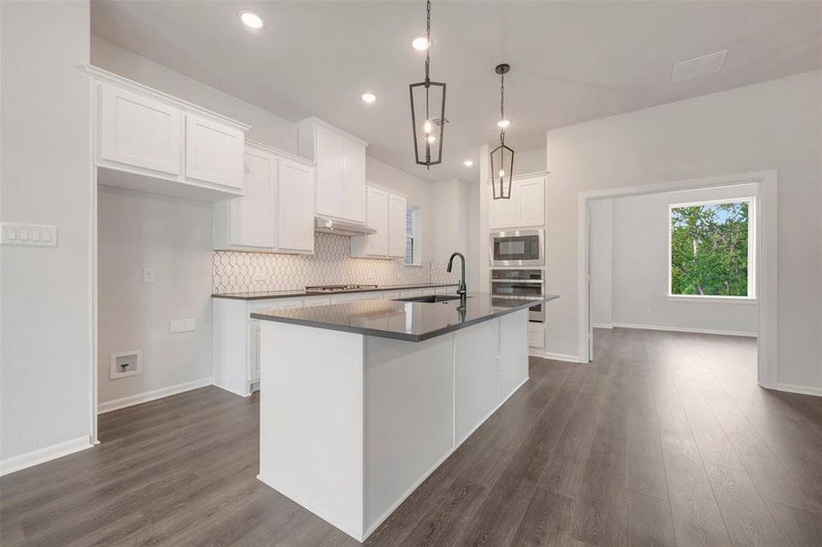 Modern kitchen featuring a central island with a matte black faucet, dark countertops, and white cabinetry Modern kitchen featuring a central island with a matte black faucet, dark countertops, and white cabinetry