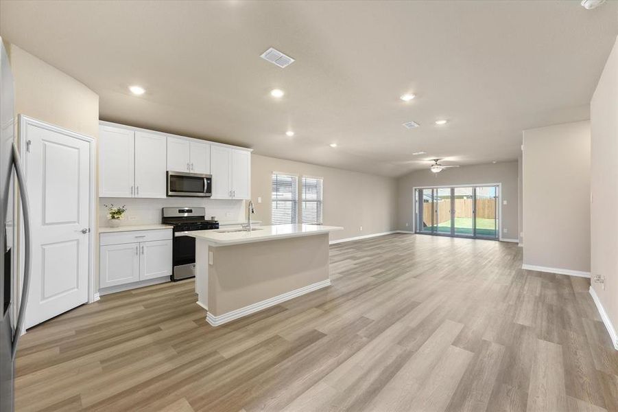 Kitchen with a center island with sink, white cabinetry, stainless steel appliances, open floor plan, and recessed lighting Kitchen with a center island with sink, white cabinetry, stainless steel appliances, open floor plan, and recessed lighting