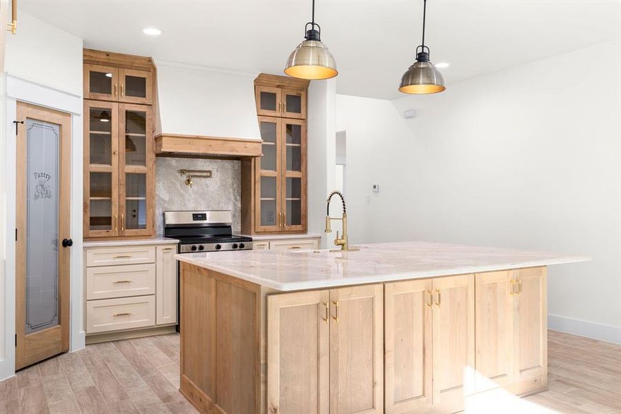 Kitchen with light brown cabinets, light wood-type flooring, a kitchen island with sink, and stainless steel range