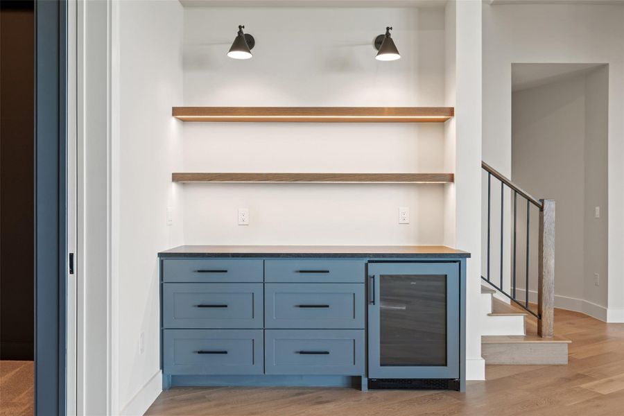 Indoor dry bar with dark countertops, blue cabinetry, wine cooler, and light wood-type flooring