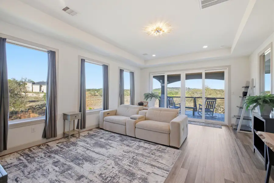 This inviting living area features light-toned flooring, a vaulted ceiling, and multiple windows that provide extensive views of the surrounding landscape