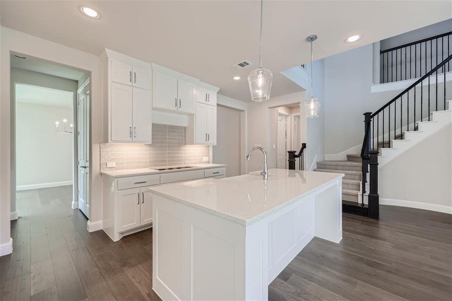 Kitchen featuring white cabinetry, dark hardwood / wood-style floors, pendant lighting, and an island with sink