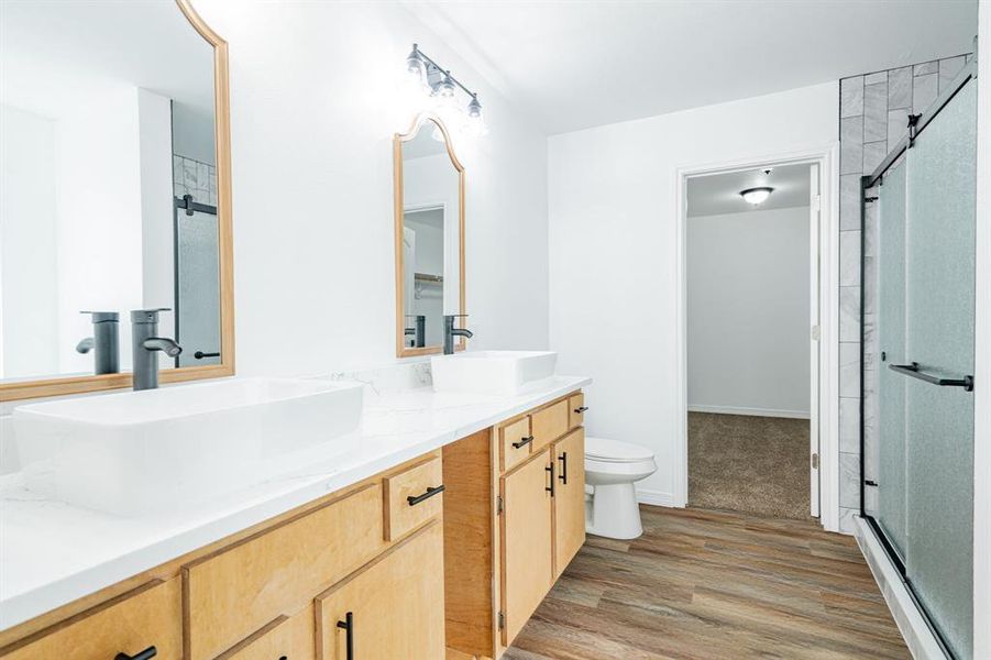 Bathroom featuring double vanity, wood-type flooring, a shower with shower door, and toilet