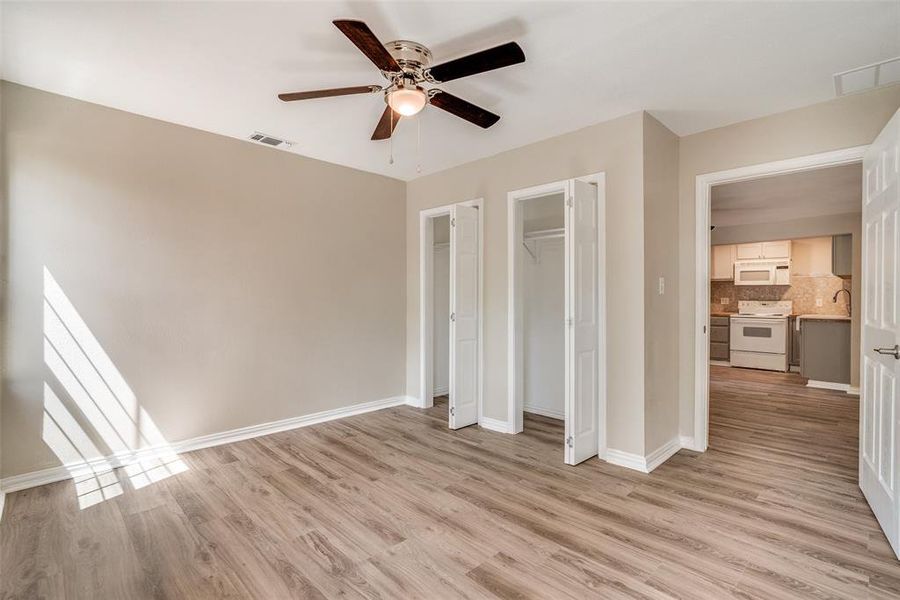 Unfurnished bedroom with multiple closets, light wood-style floors, and ceiling fan Unfurnished bedroom with multiple closets, light wood-style floors, and ceiling fan