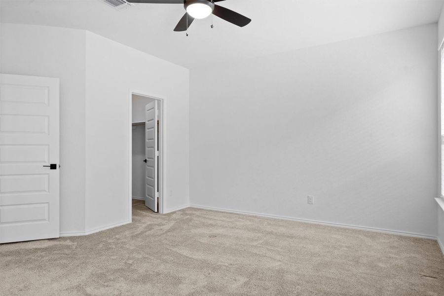 Unfurnished bedroom with a spacious closet, light colored carpet, and ceiling fan