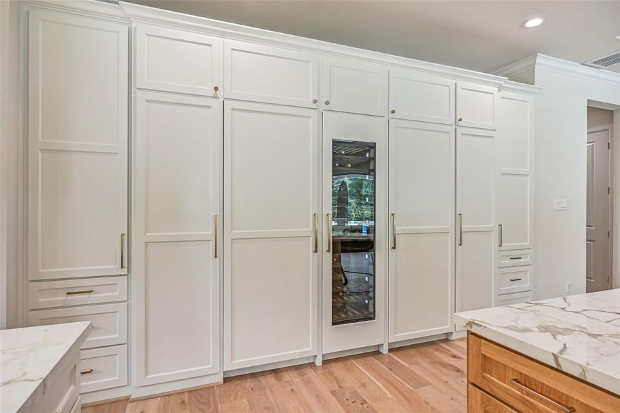 An impressive wall of floor-to-ceiling cabinetry seamlessly incorporates the paneled refrigerator & freezer with a built-in glass-front wine refrigerator centered between them, plus additional cabinetry and drawers for exceptional storage.